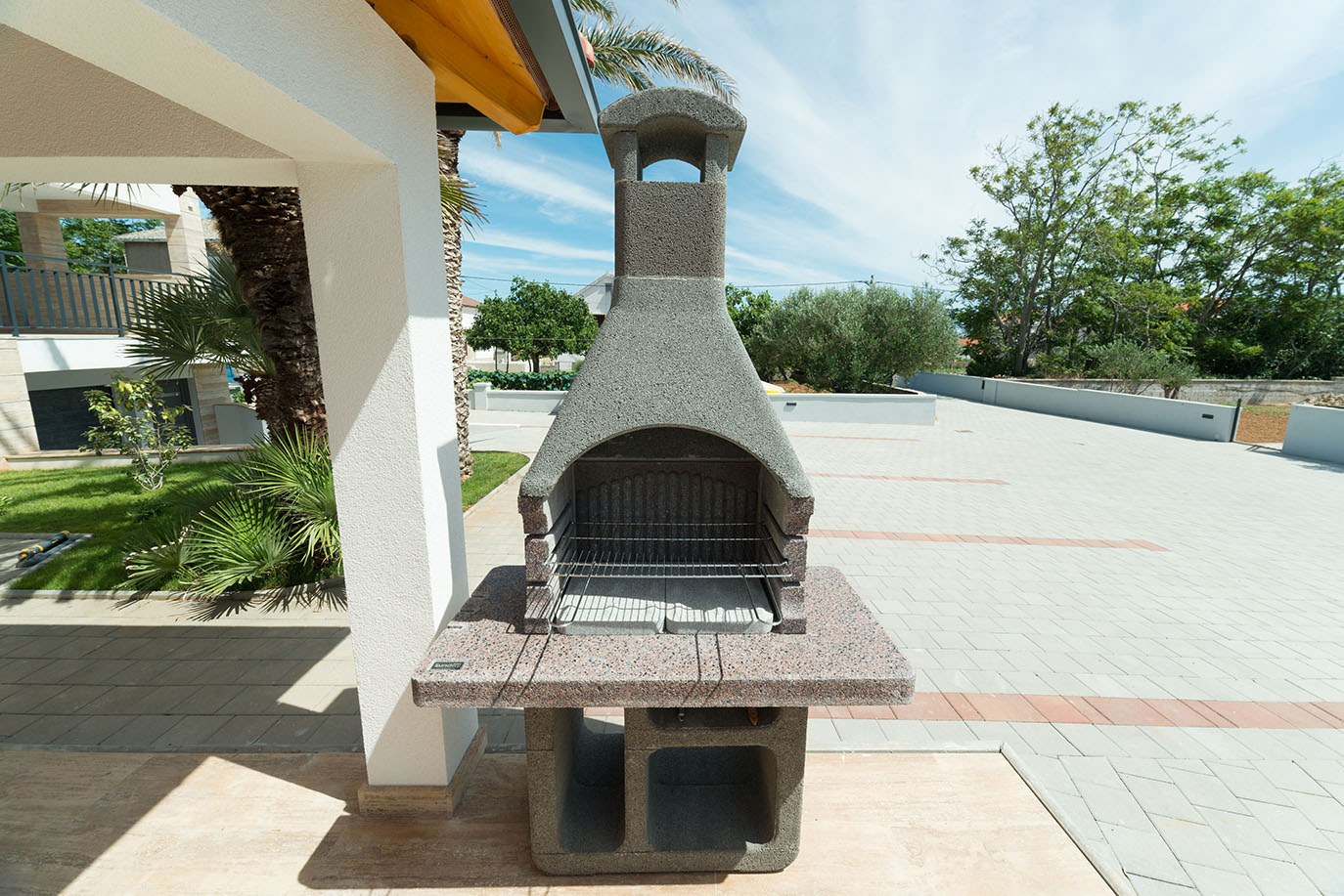 Vanjski kameni roštilj s dimnjakom i granitnom radnom pločom na popločanoj terasi, idealan sadržaj za goste apartmana Vir