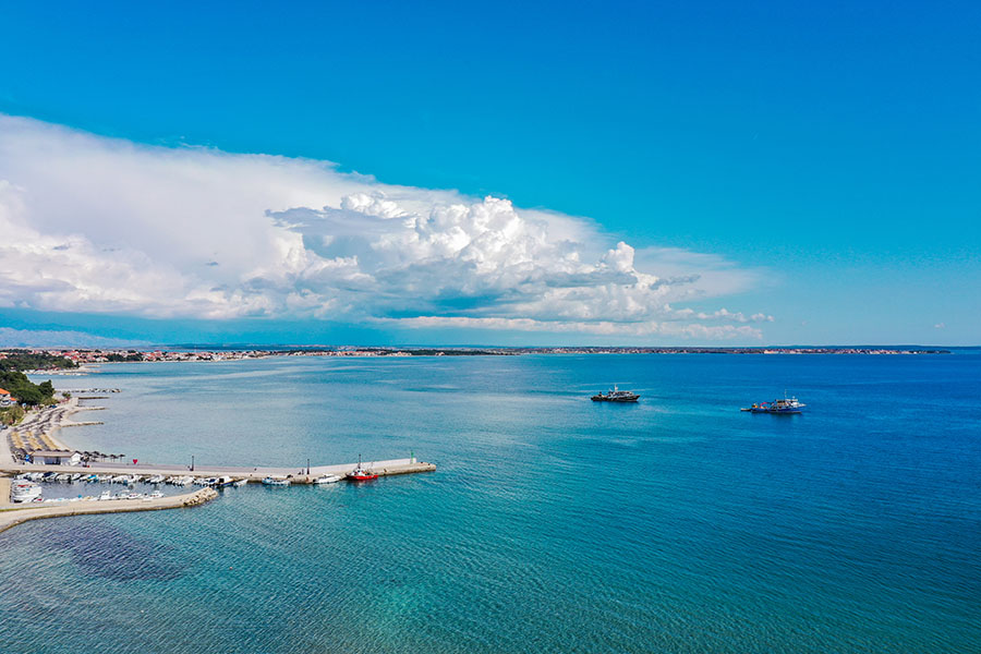 Aerial panorama of the blue bay and promenade on Vir Island with dramatic white clouds on the horizon