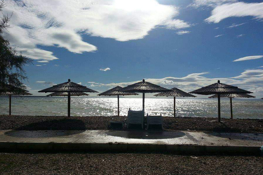 Pebble beach on Vir Island with a row of straw parasols and shimmering sea in the background