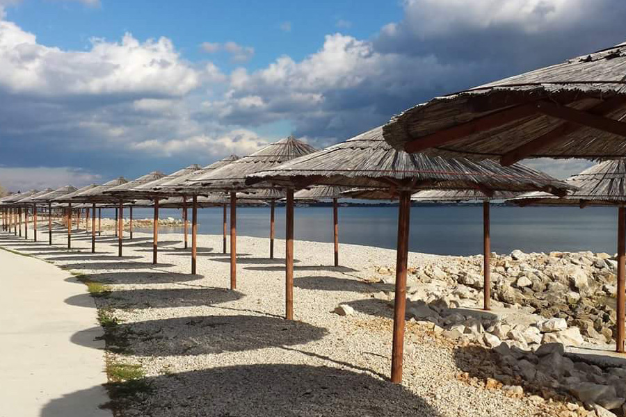 Long row of straw parasols along the walkway and calm sea on Vir Island