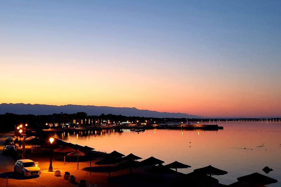 Sunset over the harbor and beach on Vir Island, with warm shoreline lights