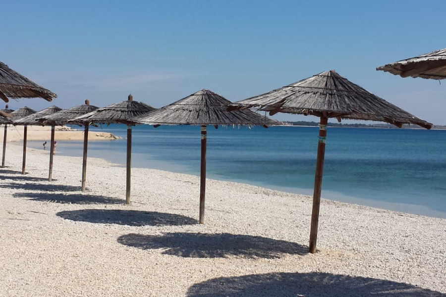 Wide pebble beach with straw parasols by turquoise water on Vir Island