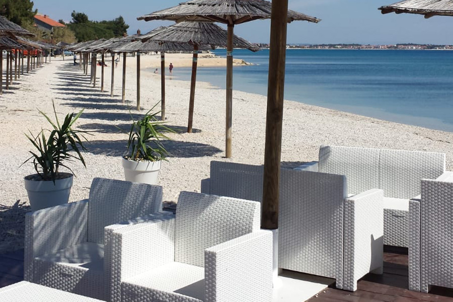 Beach bar lounge seating with a row of parasols and vivid blue sea on Vir Island